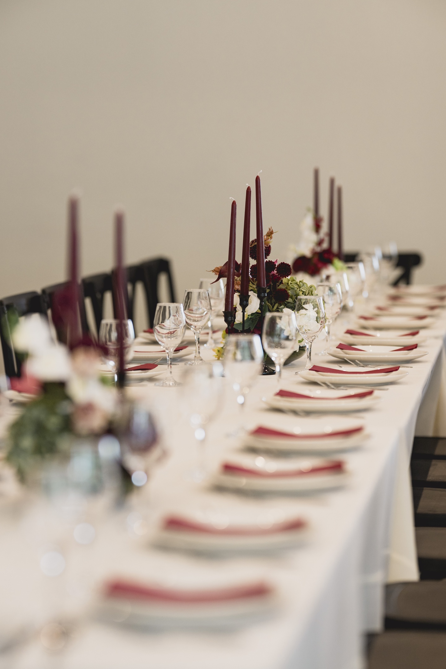 Decorated wedding tables with white tablecloths, floral arrangements, and white candle centerpieces, elegant festive setup